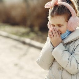 Little girl covering her nose while outside.