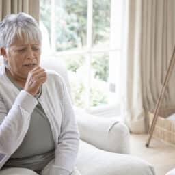 Older woman coughing while sitting in her living room at home.