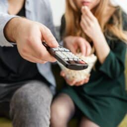 Close up of a couple watching TV with the man pointing the remote.
