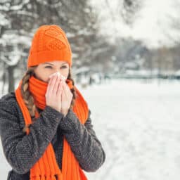 Young woman outside in the park in winter blowing her nose.
