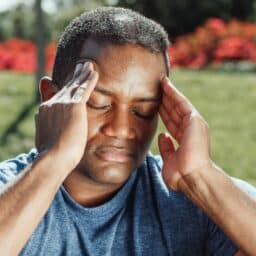 Man sitting outside suffering with a headache.