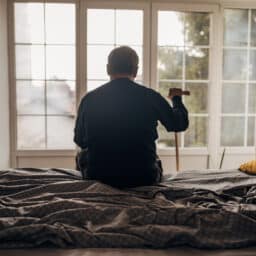 Sad man sitting on a bed looking out towards the window.