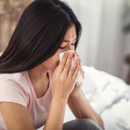 Young woman blowing her nose into a tissue at home.