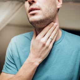 Young man touching his sore throat.
