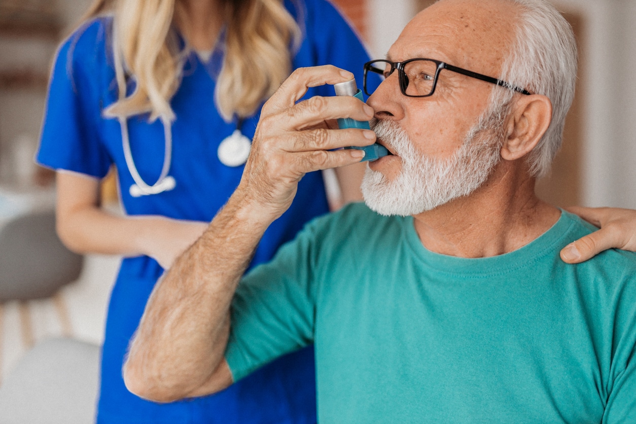 Senior man using an asthma inhaler.